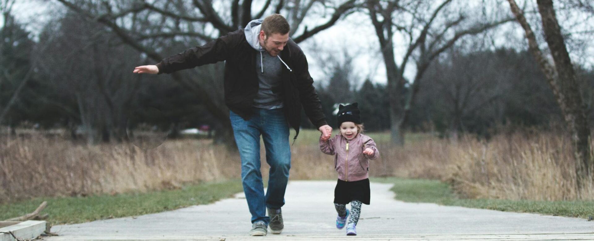 a father and his little girl running on a park pathway